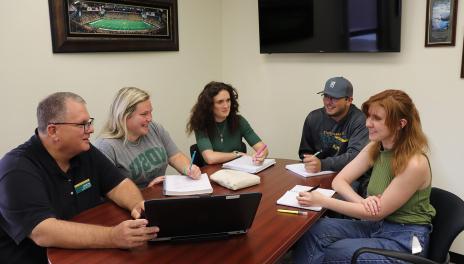 five people sitting around a table in a meeting 